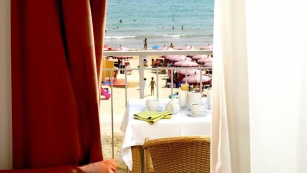 A beach view from a room with a table set for breakfast, including plates, cups, and a bottle. - Casa del Mar (Roseto degli Abruzzi)