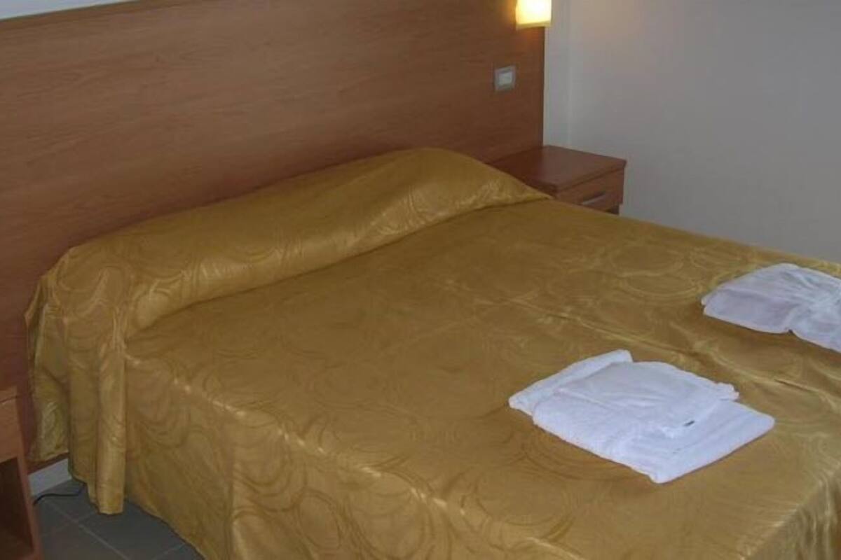 Un lit bien fait, recouvert d’une couvre-lit dorée, avec deux serviettes blanches pliées posées dessus.