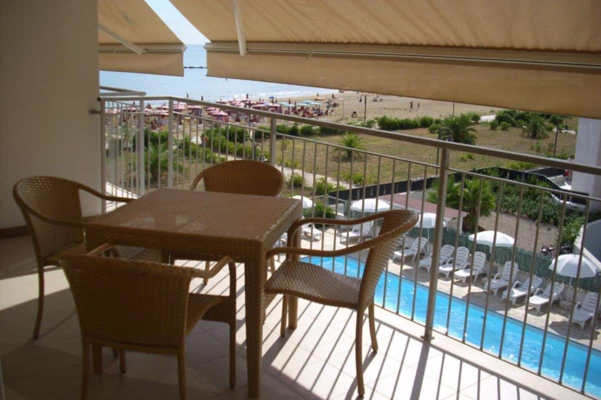 Un balcon doté de meubles en osier, donnant sur une piscine et une plage.
