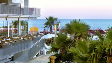 Un ristorante sul mare con posti a sedere all'aperto e vista sull'oceano, dotato di un balcone con ringhiera e vista sulla spiaggia.