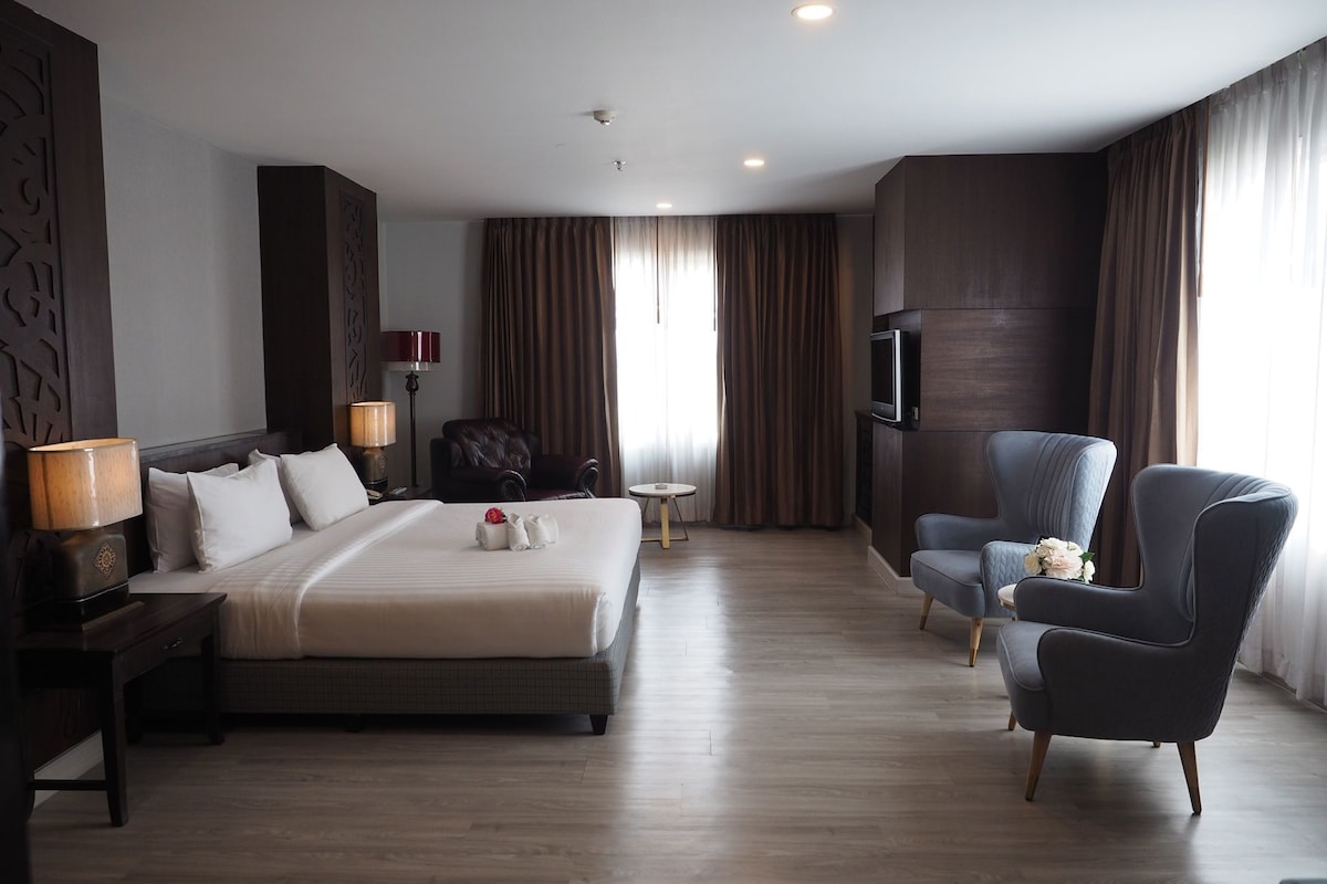 Une chambre d’hôtel avec un grand lit, un bureau, une chaise, une télévision et une fenêtre avec des rideaux.