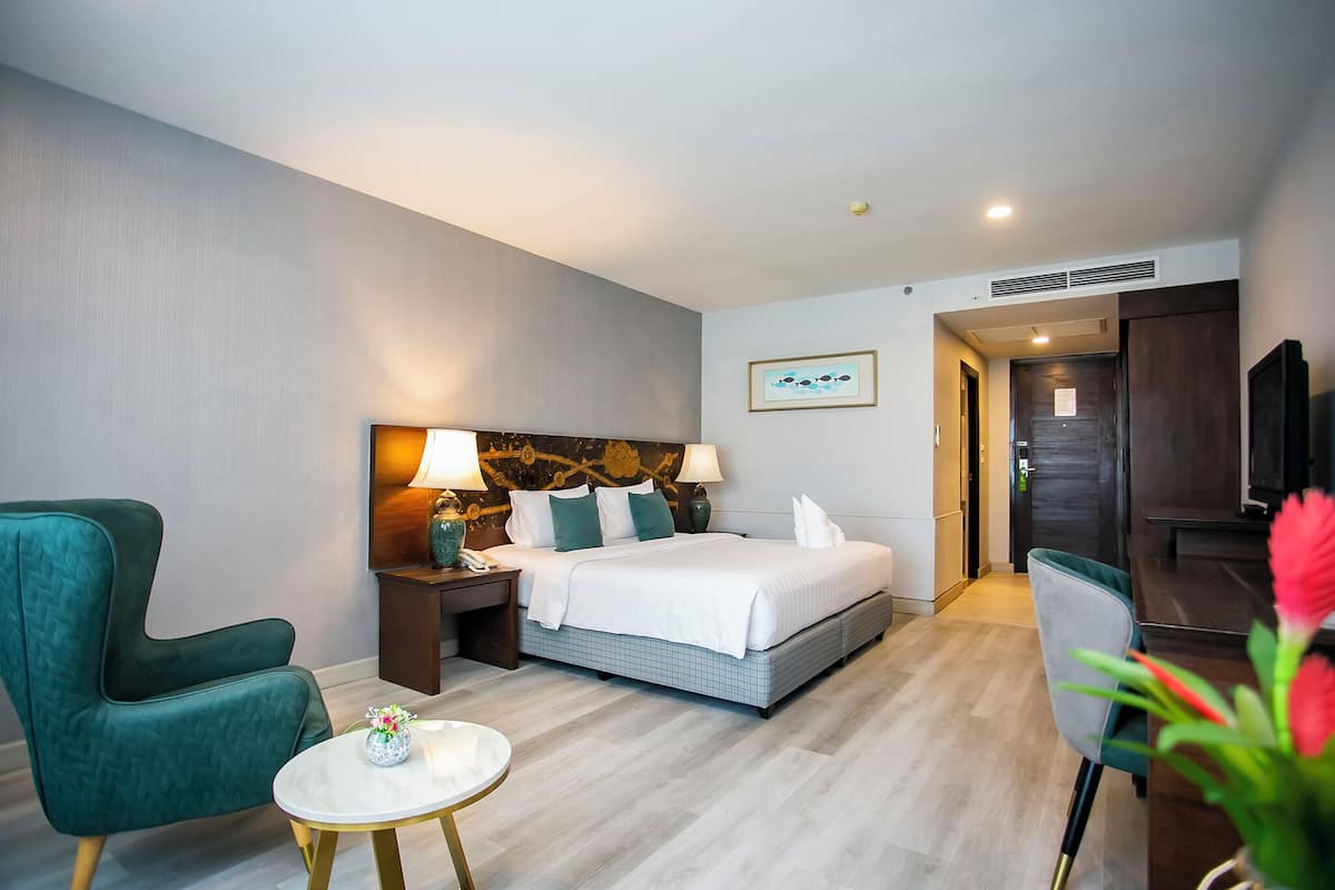 Hotellihuoneessa on sänky, kaksi yöpöytää, vihreä nojatuoli, pieni pyöreä pöytä ja televisio.