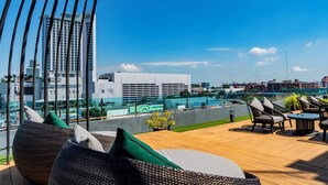 Um terraço com área de estar em vime, piscina e vista para edifícios da cidade.