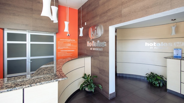 A hotel reception area with a curved counter, a wooden wall, and a reception desk. - Hotel Hi! Zapopan (Zapopan)