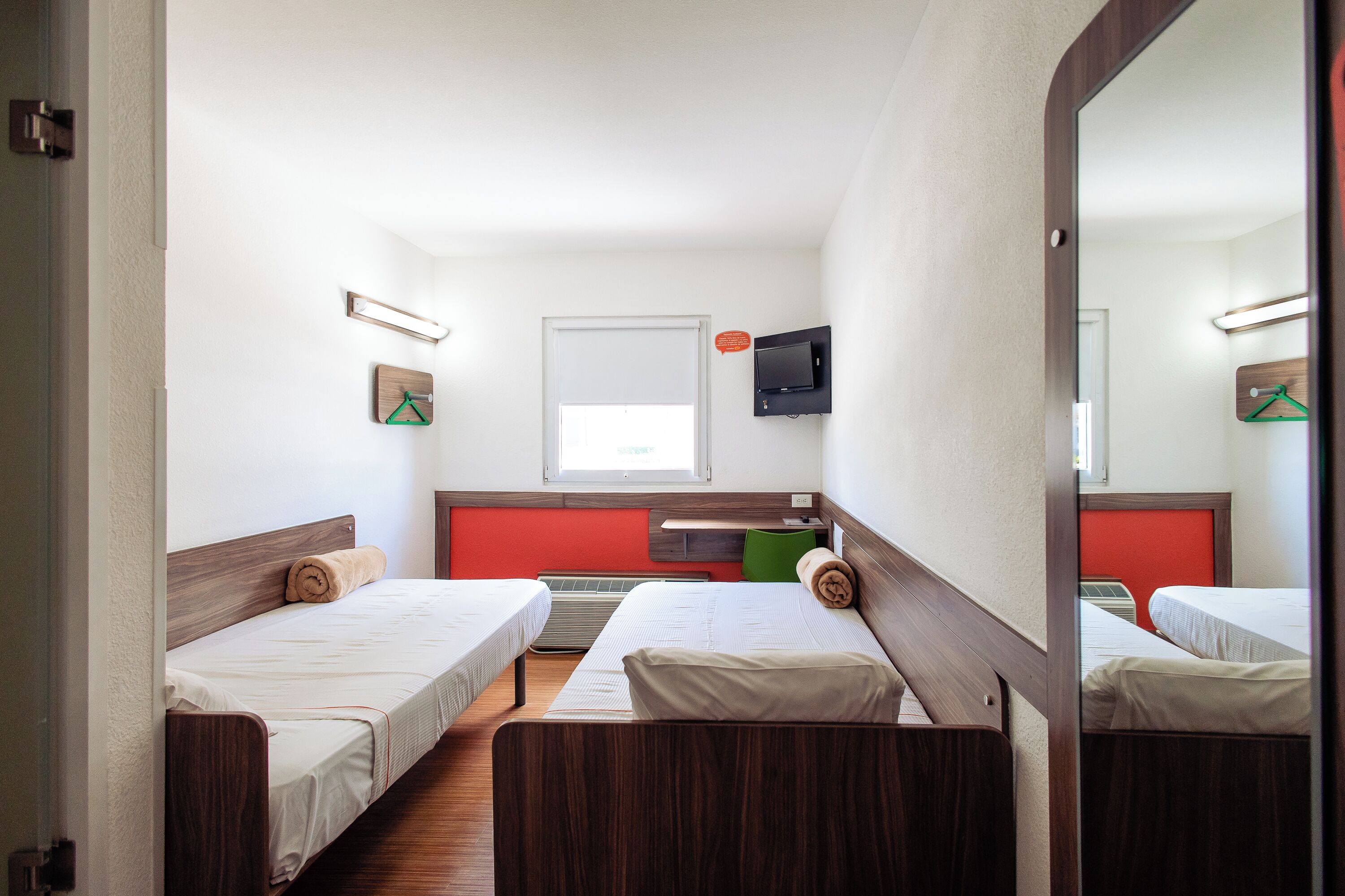 A room with two single beds, a small desk, a mirror, and a television.