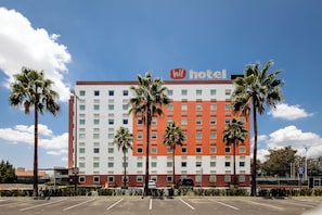 Un hotel con fachada roja y blanca, palmeras en primer plano y un cielo azul despejado.