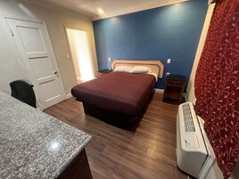 Habitación de hotel con cama, escritorio, silla, calefactor y puerta.