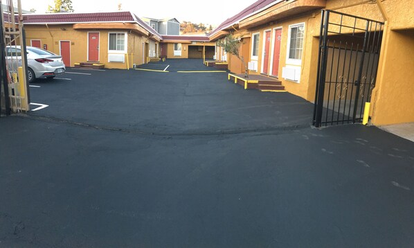 Een motel met een parkeerplaats, meerdere kamers met rode deuren en een hekwerk.