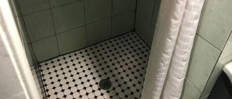 A small, tiled shower area with a drain in the center and a curtain partially visible.