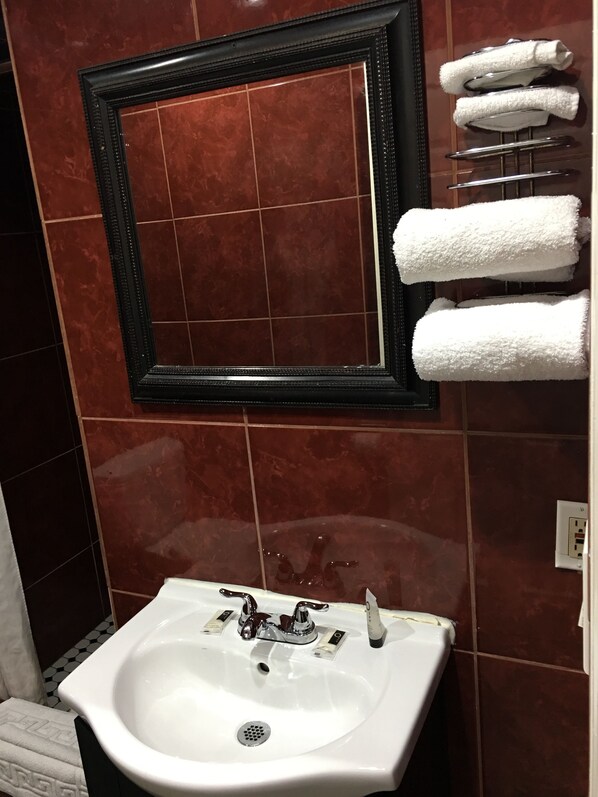 A bathroom with a white sink, a mirror, and a towel rack with towels. - Harris Motel (Oakland)