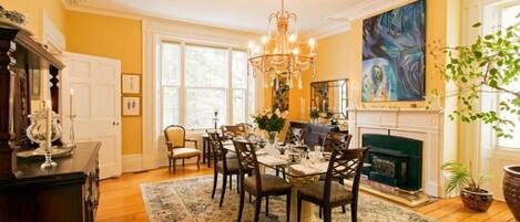 Un comedor con candelabro, chimenea y un cuadro grande en la pared.
