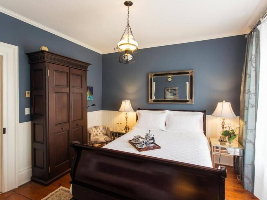 A bedroom with a large bed, two bedside tables with lamps, a wardrobe, and a chandelier.