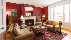 A living room with a fireplace, leather sofas, a coffee table, and a large window. - Historic Lyons House (Niagara-on-the-Lake)