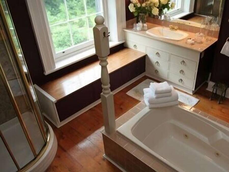 Un baño con una bañera grande, un tocador con espejo y una ventana con vistas al verdor.