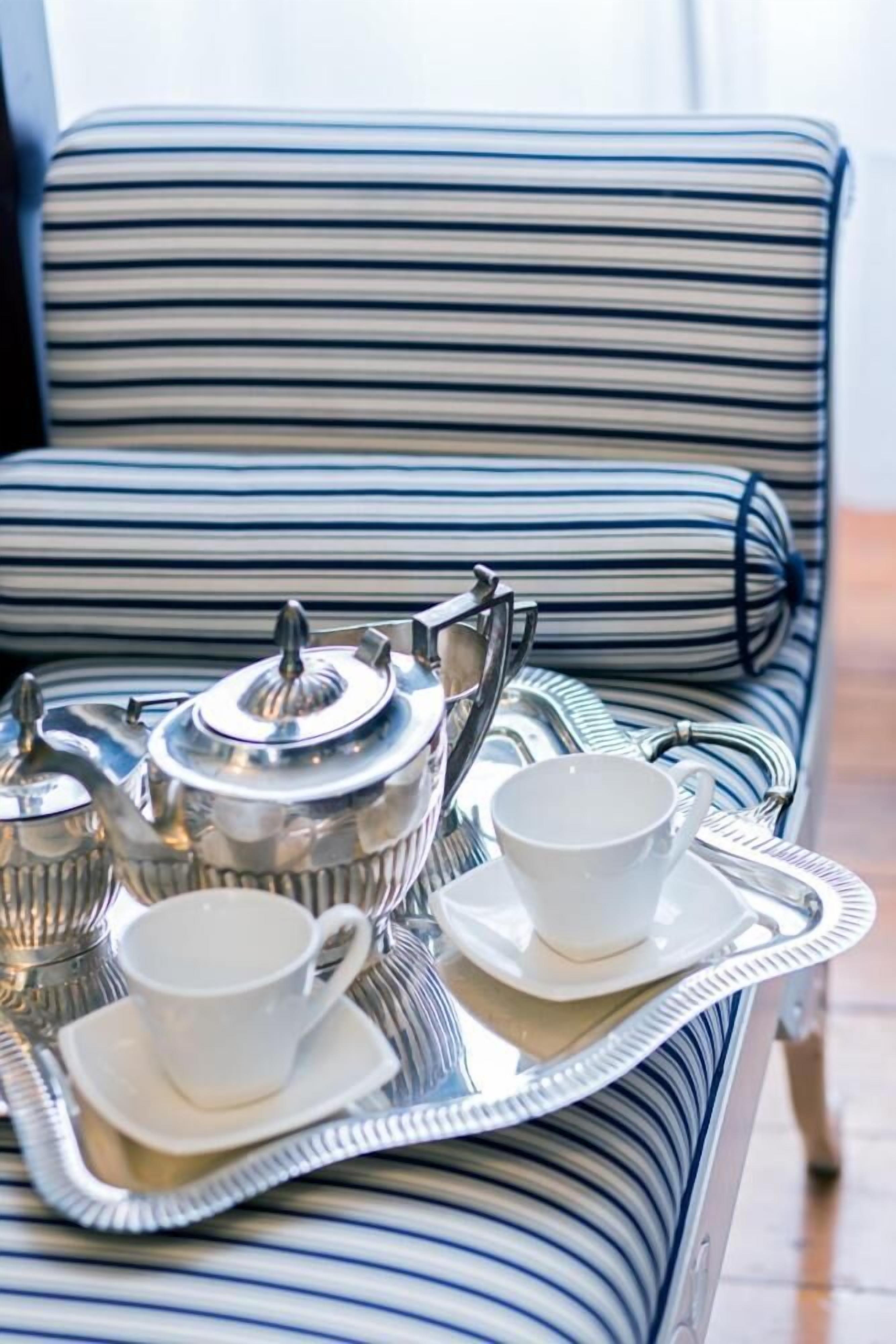 A striped sofa with a tray holding a teapot, cups, and saucers.