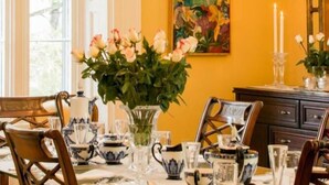 A dining area with a chandelier, table set with glassware, and a vase of flowers. - Historic Lyons House (Niagara-on-the-Lake)