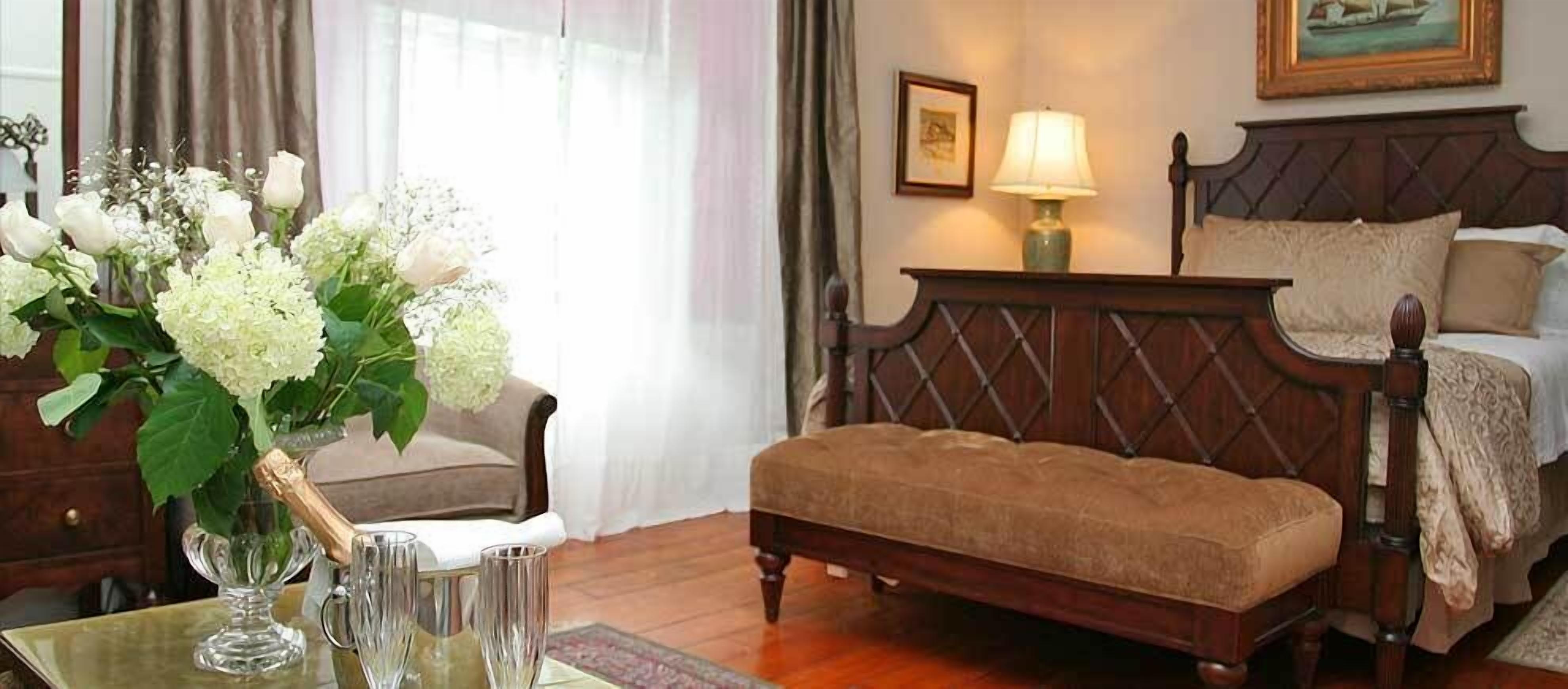 A bedroom with a wooden bed, a bedside table with a lamp, and a vase with flowers.