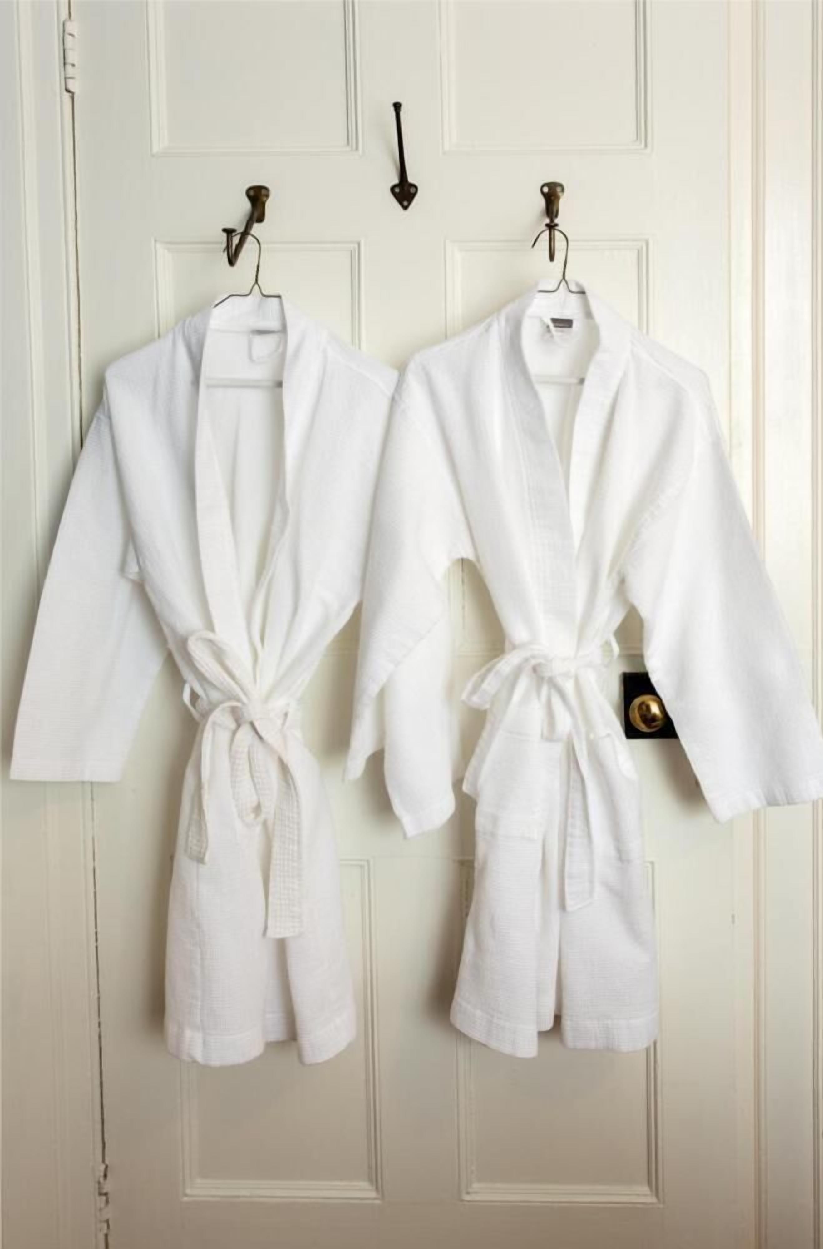 Dos albornoces blancos colgados en una puerta con un tirador de latón.