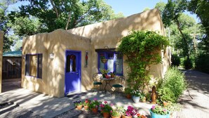 A small, single-story building with a blue door and windows, surrounded by potted plants and a small table with chairs.