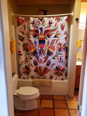 Une salle de bain avec un rideau de douche coloré, des toilettes blanches et une serviette jaune accrochée au mur.