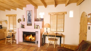 A cozy living room with a fireplace, wooden beams, a dining area, and a patterned sofa.