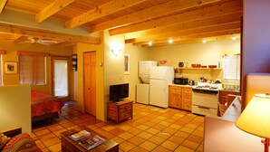 A cozy living room with a sofa, a coffee table, and a TV. The kitchen has wooden cabinets, a refrigerator, and a stove.