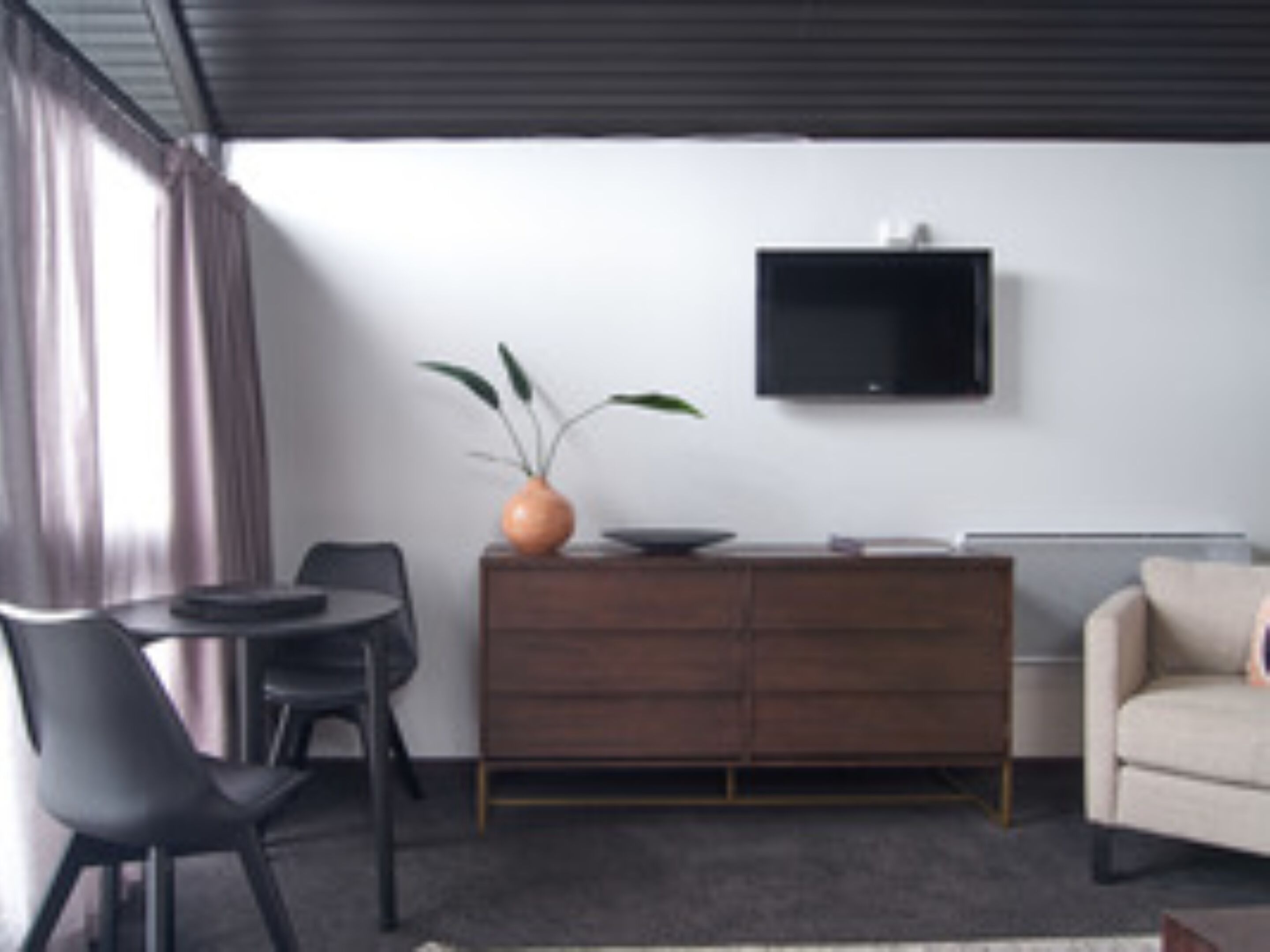 Un salon moderne comprenant un canapé, un téléviseur fixé au mur, un meuble en bois et un coin repas avec des chaises et une table.