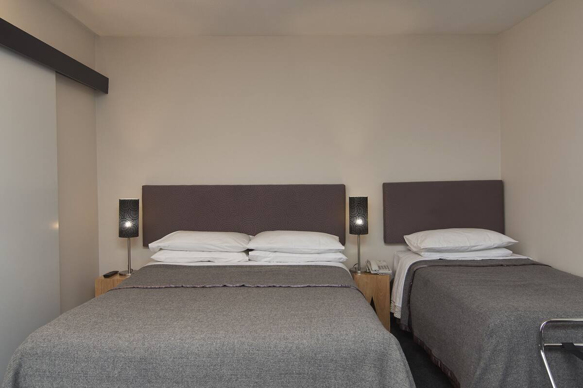 A hotel room with two single beds, a bedside table with a lamp, and a wall-mounted telephone.