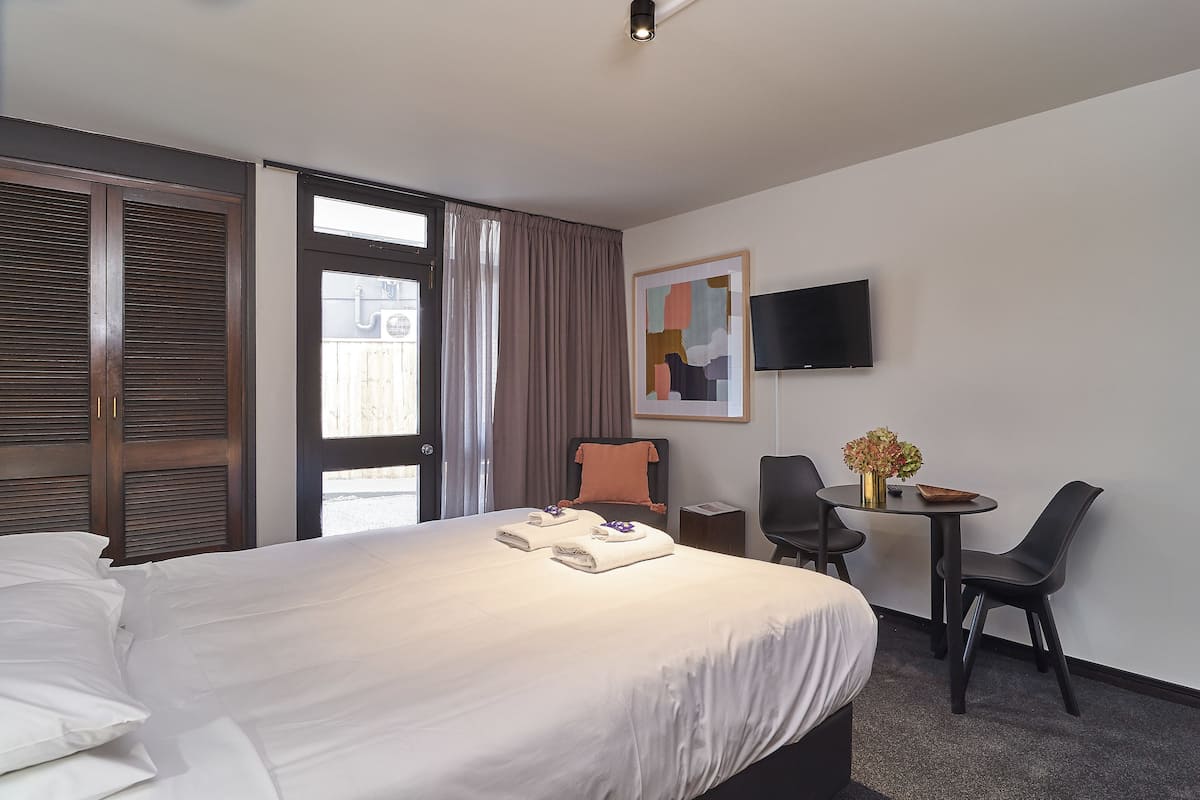 A hotel room with a large bed, a desk with a chair, a TV on the wall, and a window with curtains.