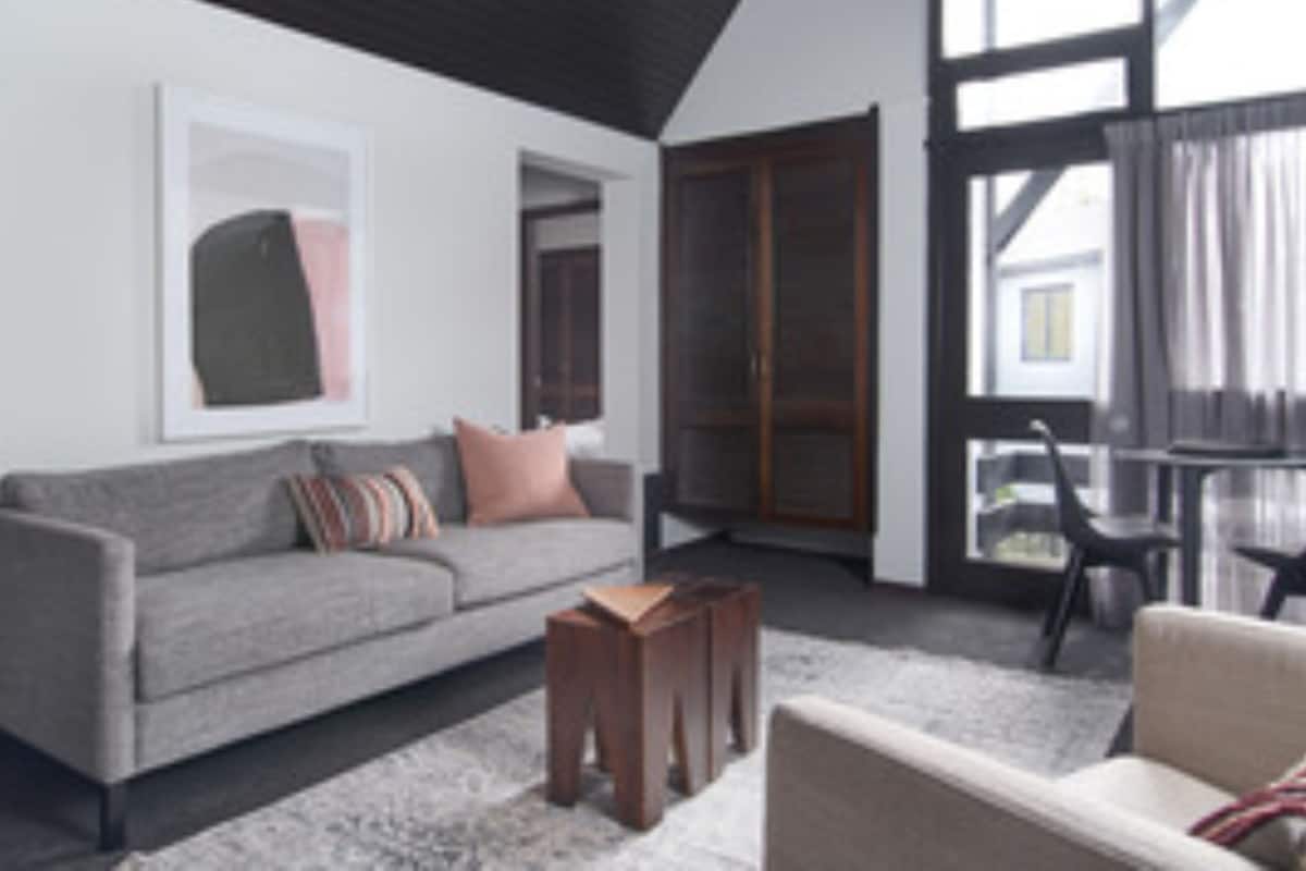 A modern living room with a grey sofa, a small wooden table, and a beige armchair.