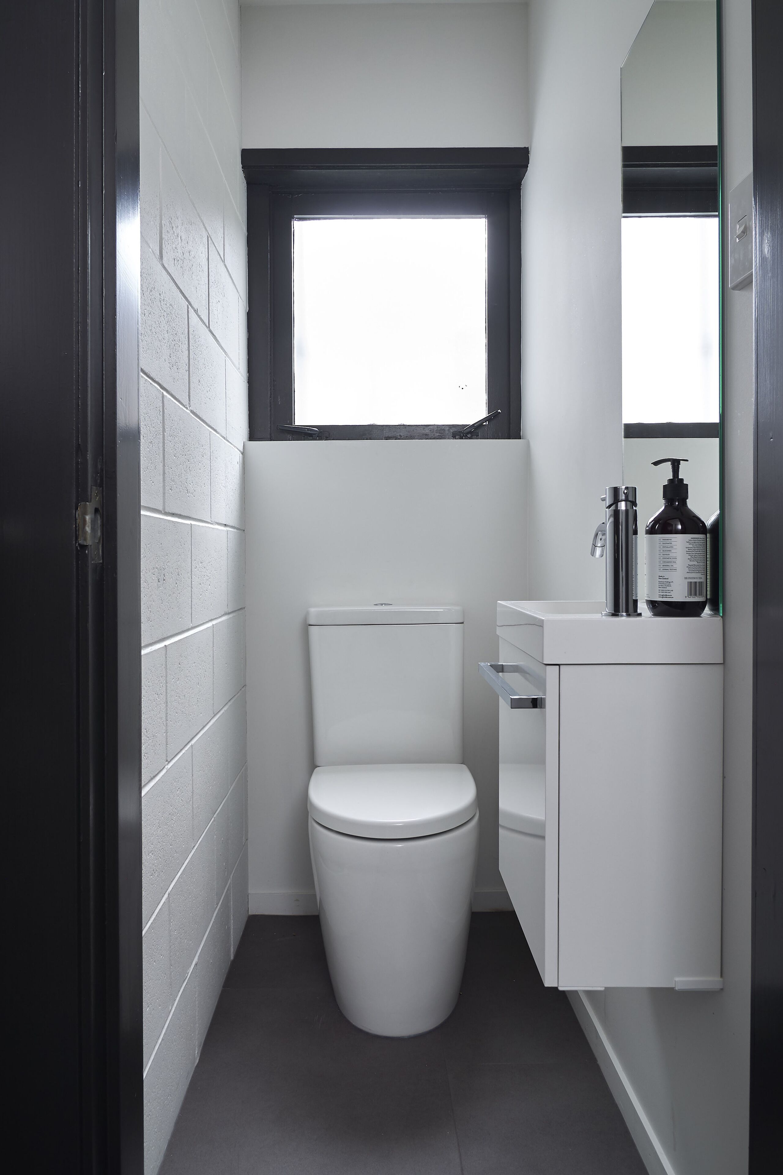Une salle de bain moderne et compacte, avec des toilettes blanches, une petite fenêtre au-dessus du lavabo et un miroir au-dessus du lavabo.