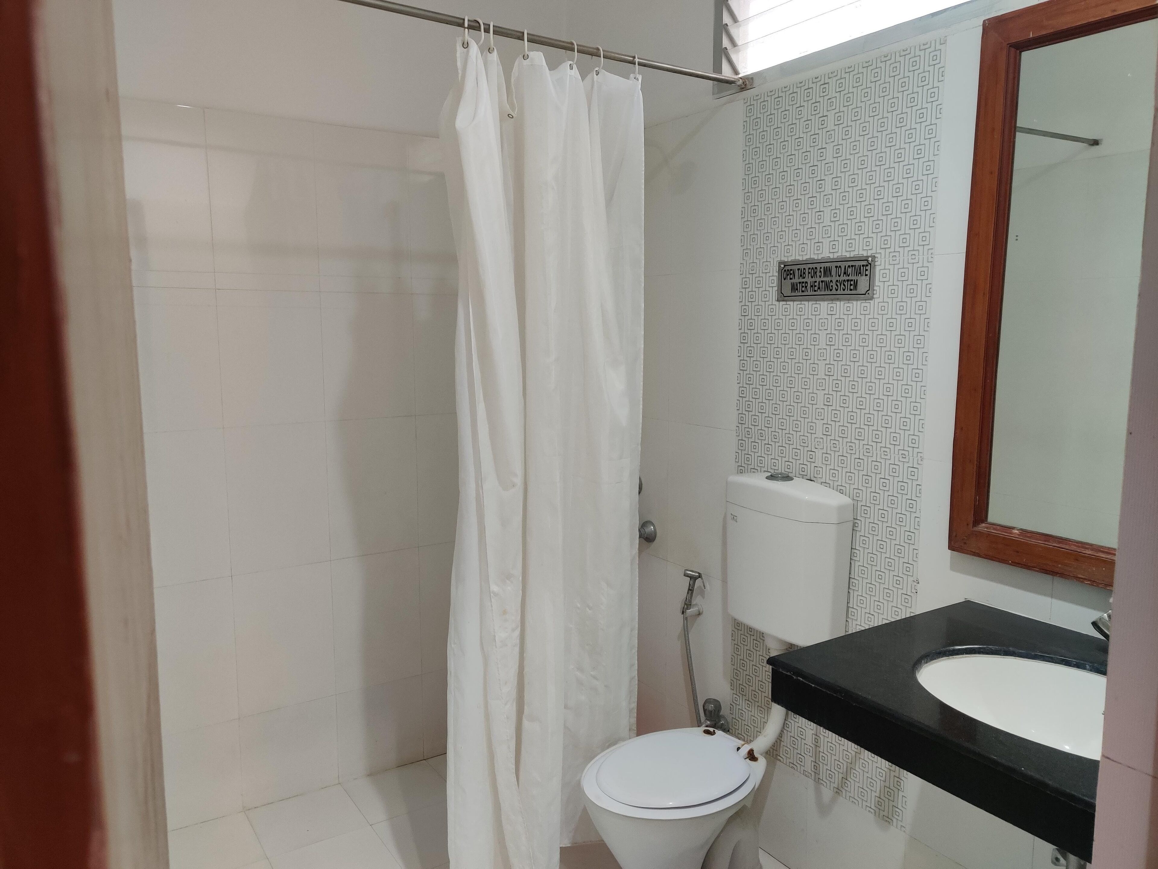 A bathroom with a white toilet, a shower curtain, a sink with a black countertop, and a mirror.