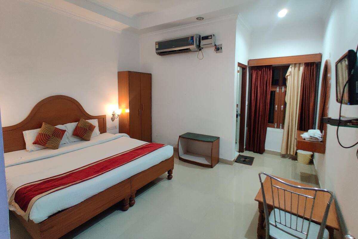 A hotel room with a bed, a desk, an air conditioning unit, a television, and a wardrobe.