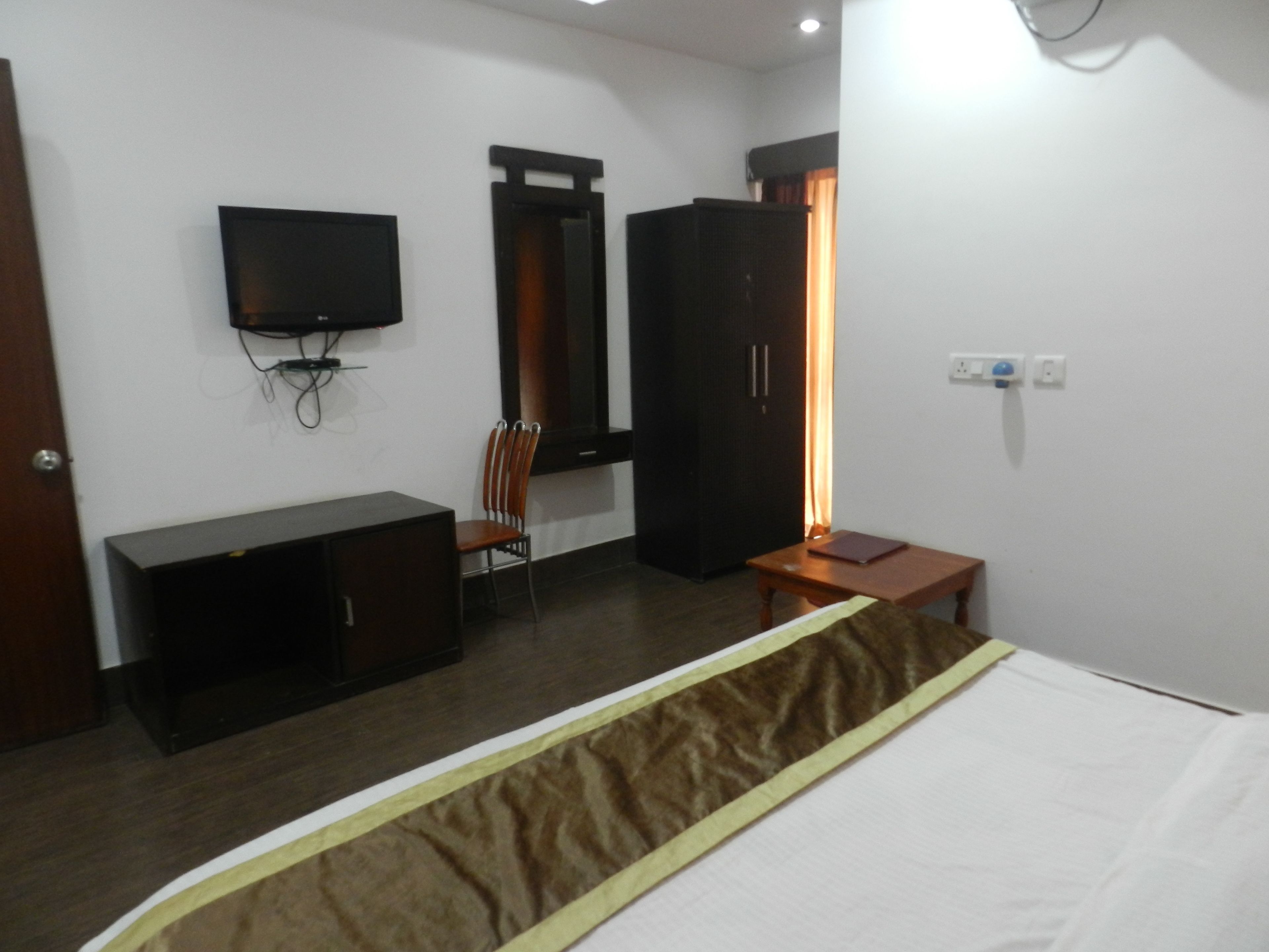 A hotel room with a bed, a desk, a chair, a wardrobe, and a television.