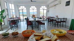 Un comedor con varias mesas y sillas, un ventanal con vistas, y comida sobre la mesa.