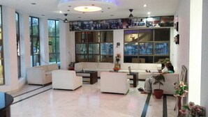 Un salón amplio con ventanas grandes, un conjunto de sofá blanco, una mesa de centro y un ordenador portátil sobre una mesita auxiliar.