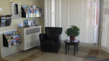 A reception area with a black leather chair, a potted plant, and a wall with various brochures and magazines.