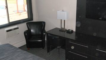 Habitación de hotel con un sillón de cuero negro, un escritorio con lámpara y un televisor grande en la pared.
