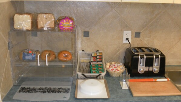 A kitchen with a toaster, a bread box, a basket of bread, and a plastic bag of bread.