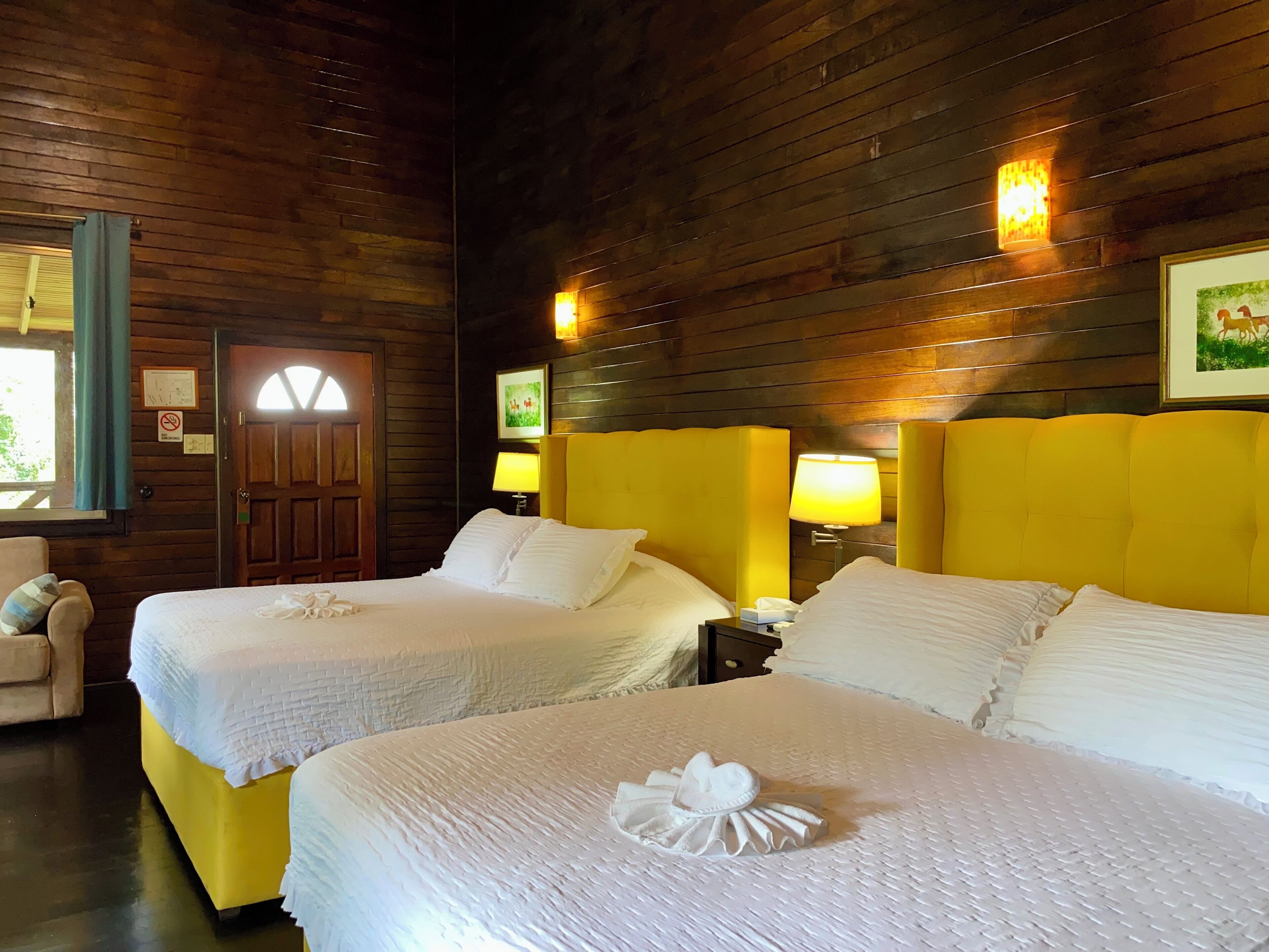 A hotel room with two beds, wooden walls, and a window with curtains.