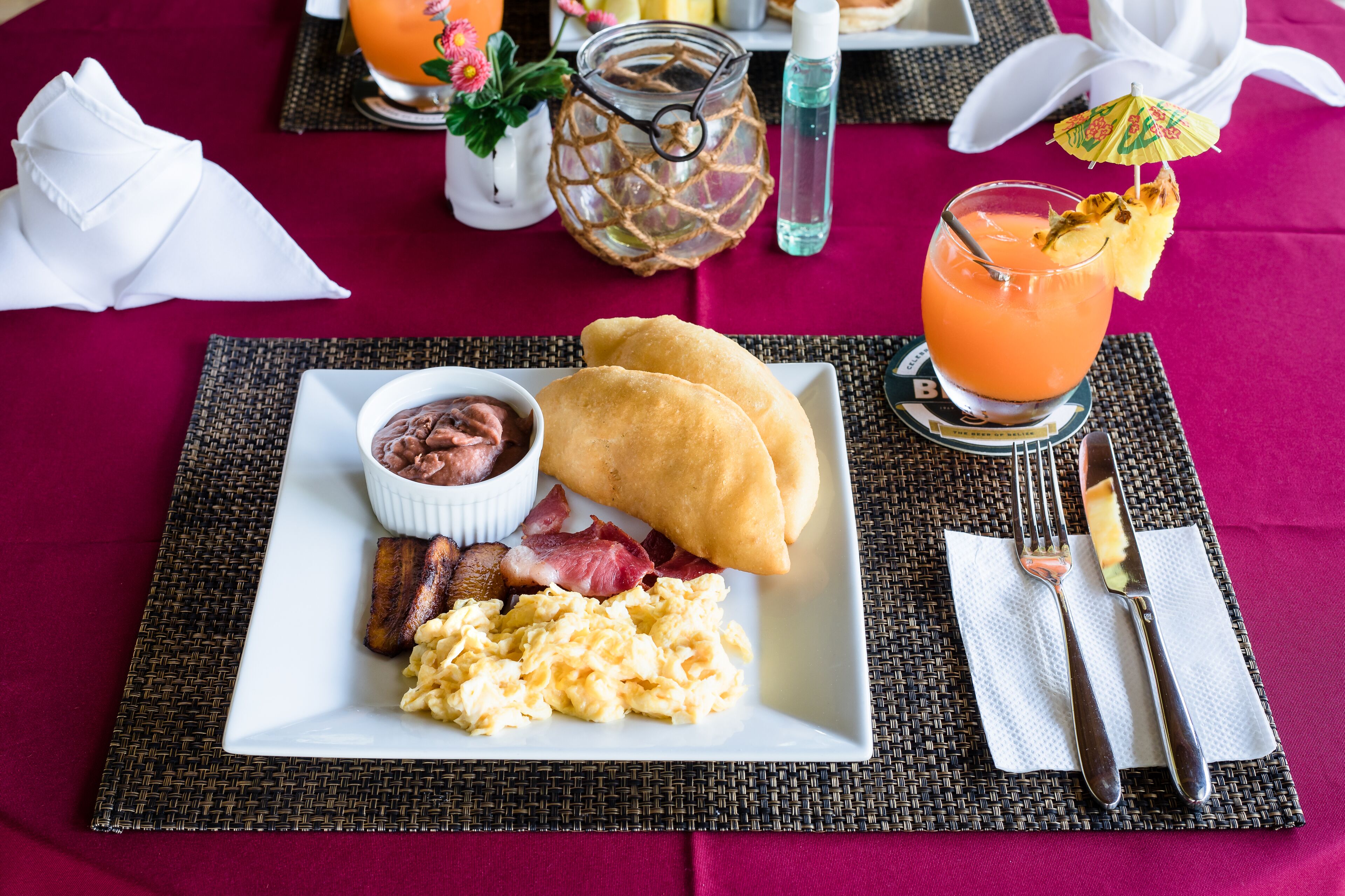 A breakfast plate with eggs, bacon, and toast, a glass of orange juice, and a small bowl of chocolate.