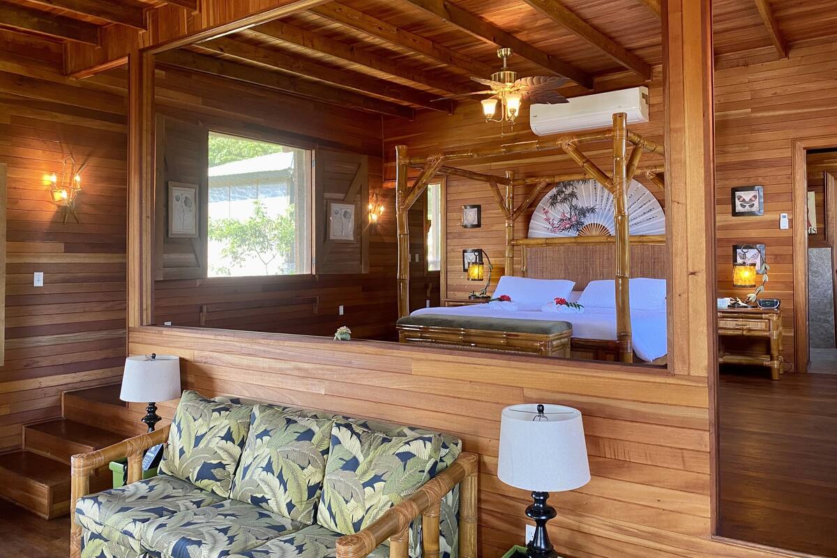 A wooden cabin with a four-poster bed, a sofa, and a dining table.
