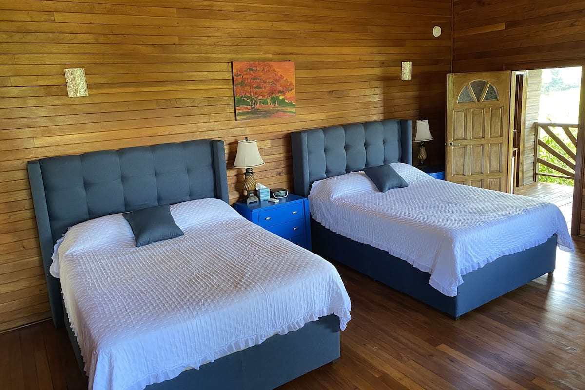 A room with two beds, wooden walls, a painting, and a door leading outside.