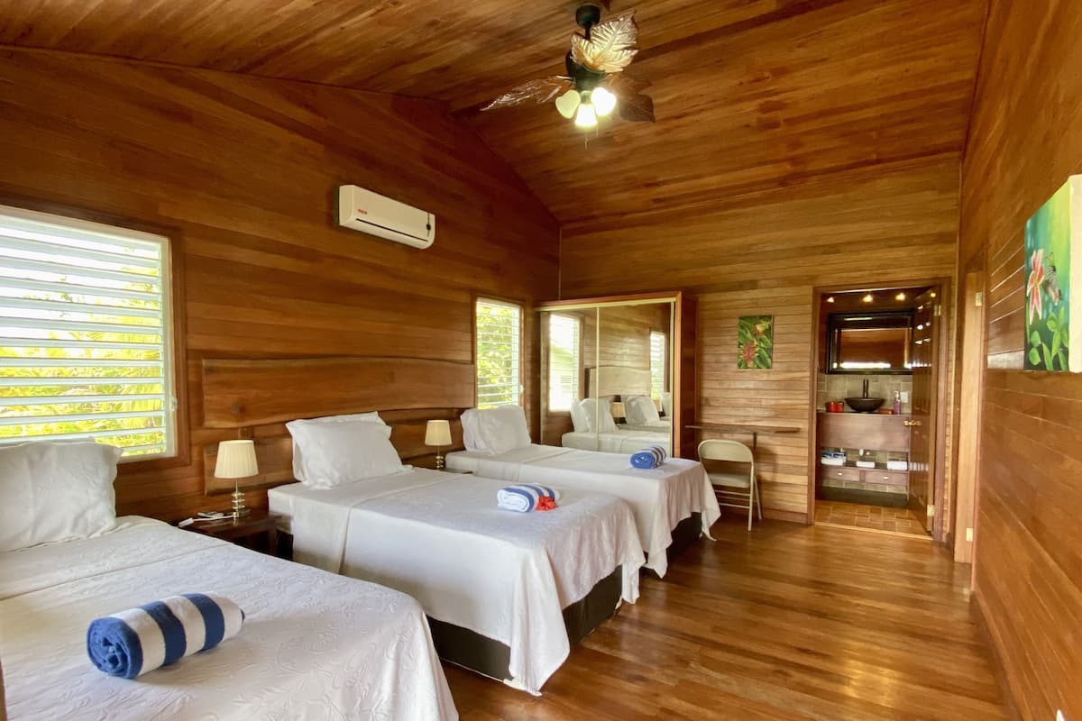 A wooden cabin with three beds, a ceiling fan, and a small kitchenette.