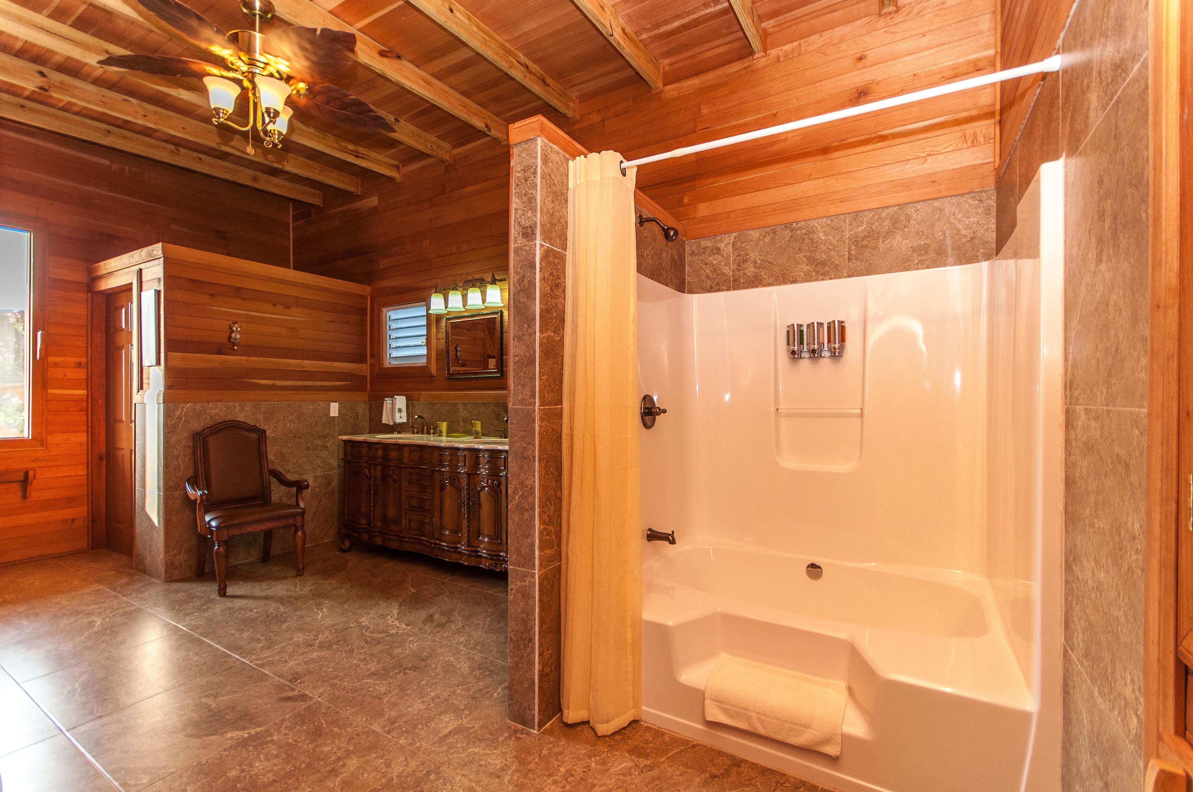 A wooden interior with a shower, a bathtub, a wooden chair, and a vanity with a sink.