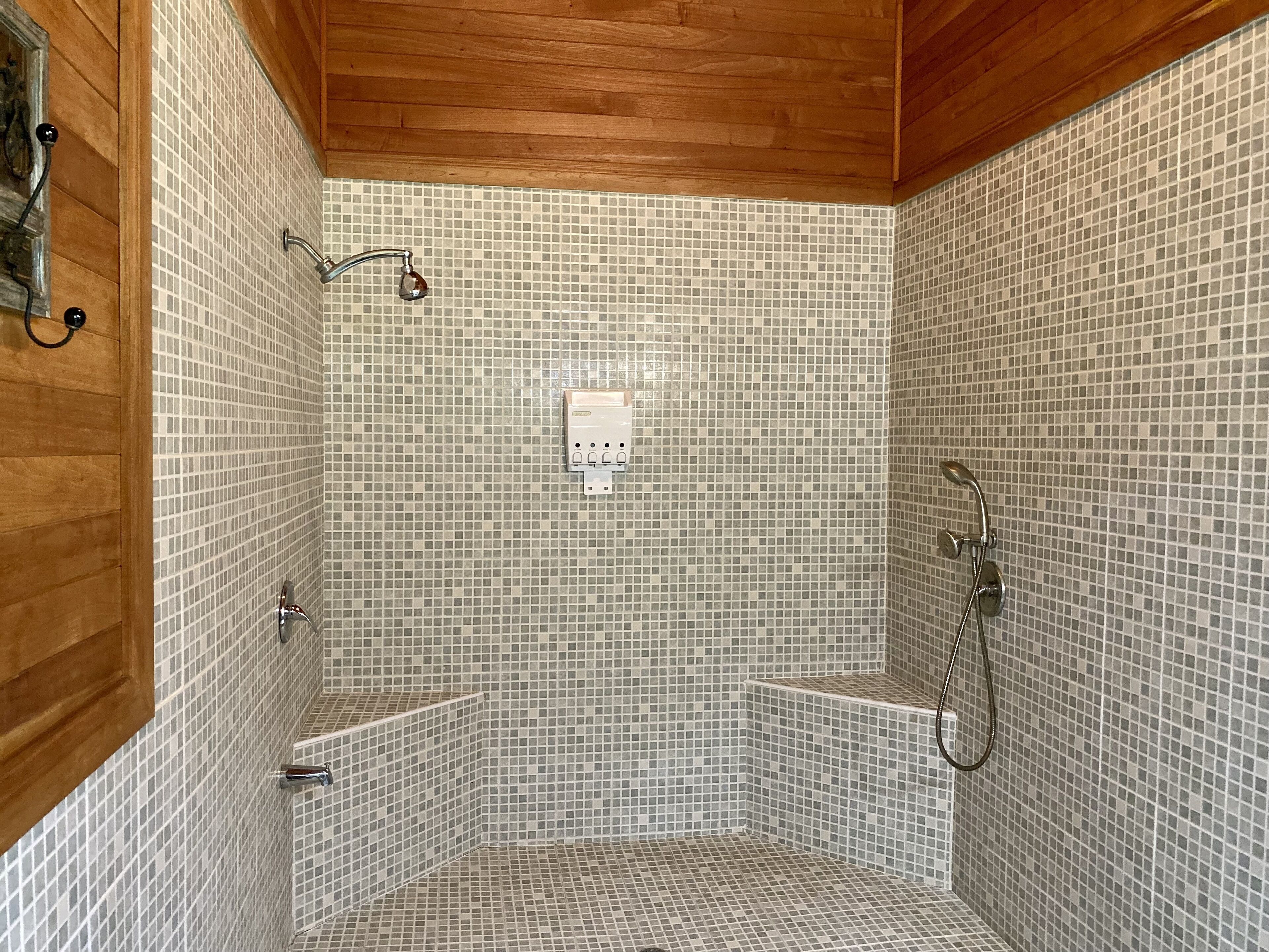 A shower with mosaic tile walls and wooden ceiling.