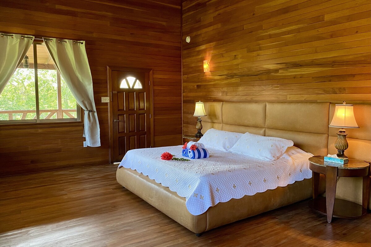 Um quarto com paredes de madeira, uma cama, duas luminárias de cabeceira e uma janela com cortinas.