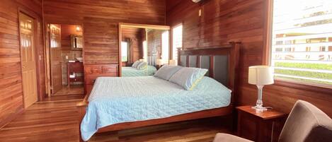 Un dormitorio tipo cabaña de madera con cama, mesita de noche, silla y ventana con vistas.