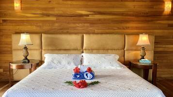 A neatly made bed with a white quilted bedspread, two pillows, and a decorative arrangement of rolled towels and flowers.