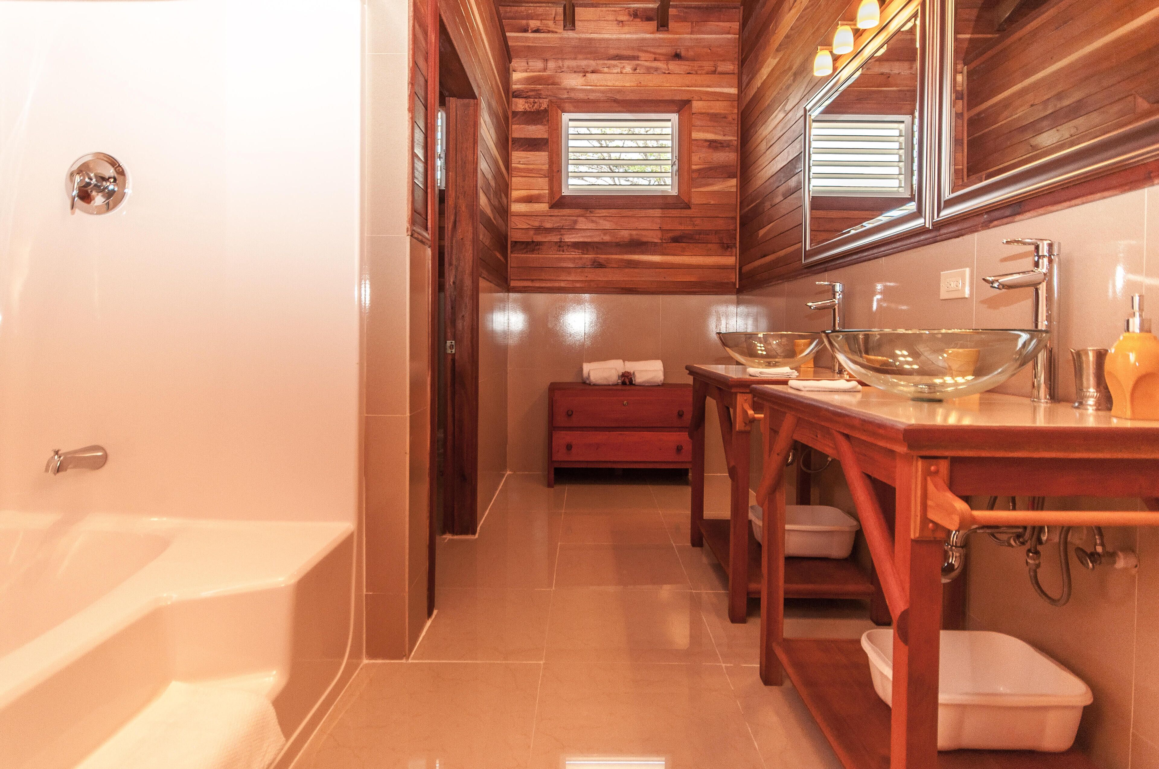 A bathroom with a wooden ceiling, a bathtub, a sink with a glass bowl, and a red cabinet.